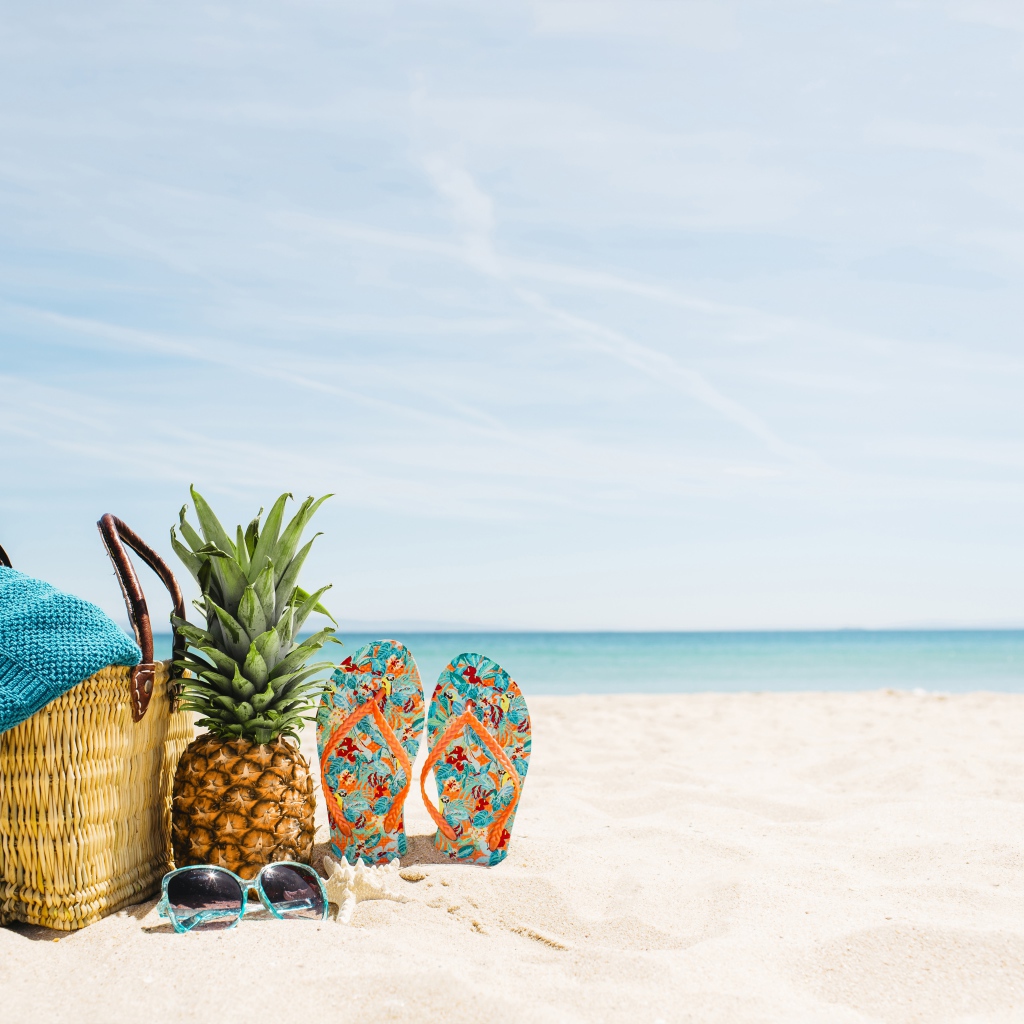 Сумка, ананас, шлепанцы и солнечные очки лежат на песке на пляже летом