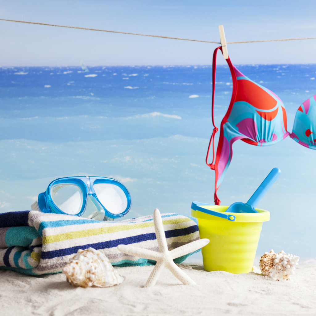 Очки, купальник, полотенце, ракушки и игрушки на песке на пляже летом