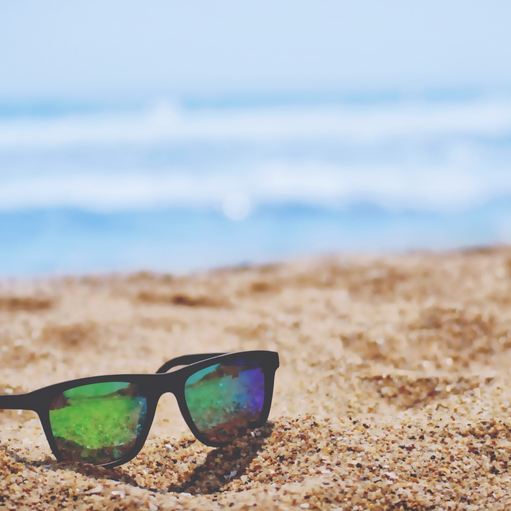 Солнцезащитные очки лежат на желтом песке у моря