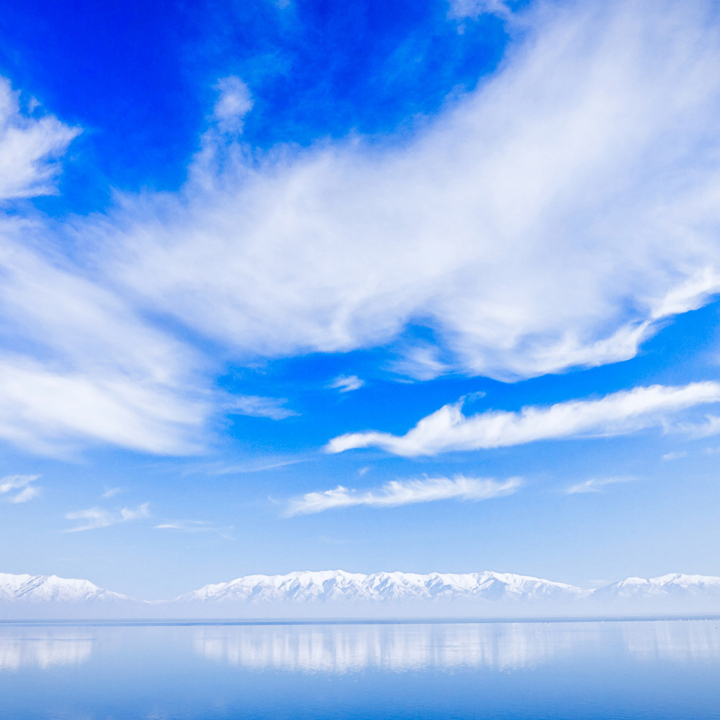 Beautiful white clouds above the water near the snow-capped mountains.