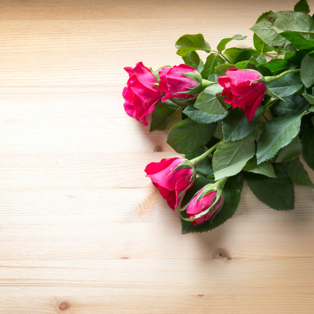 Букет розовых роз с зелеными листьями на деревянной поверхности 