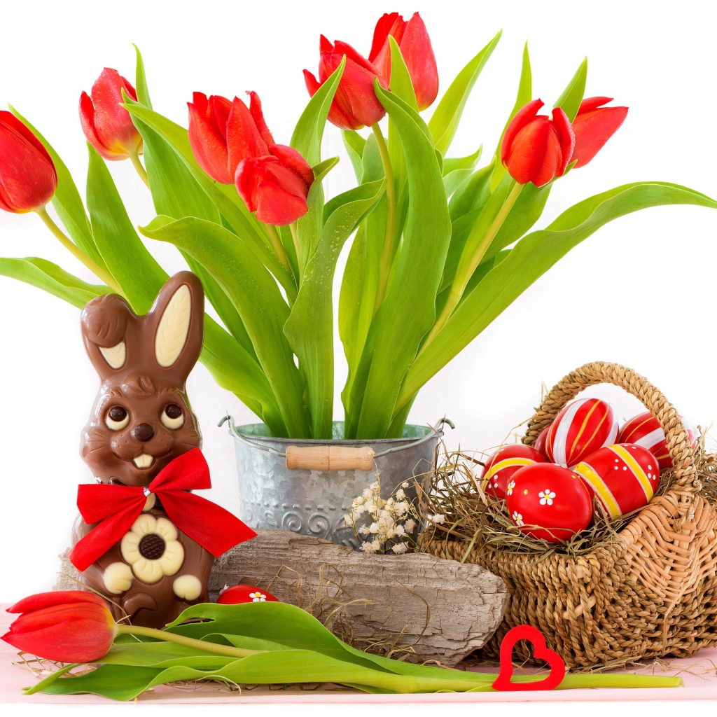 Букет красных тюльпанов на столе с шоколадным кроликом и крашеными яйцами на Пасху