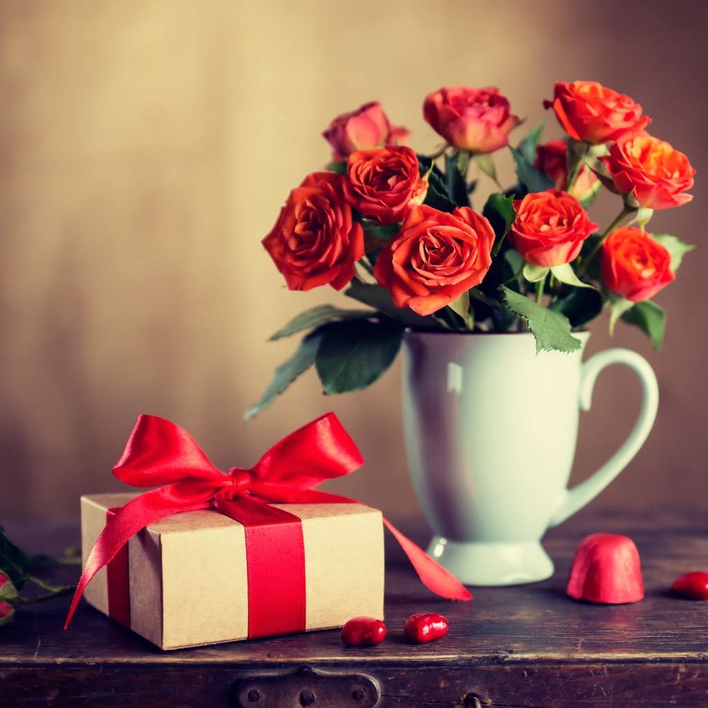 Букет роз в белой вазе с подарком на столе