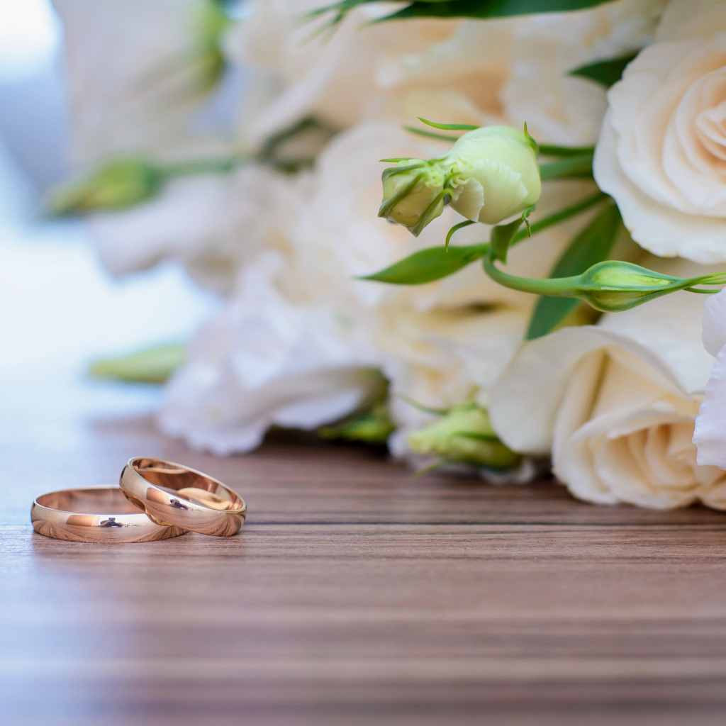 Букет белых роз на столе с золотыми обручальными кольцами