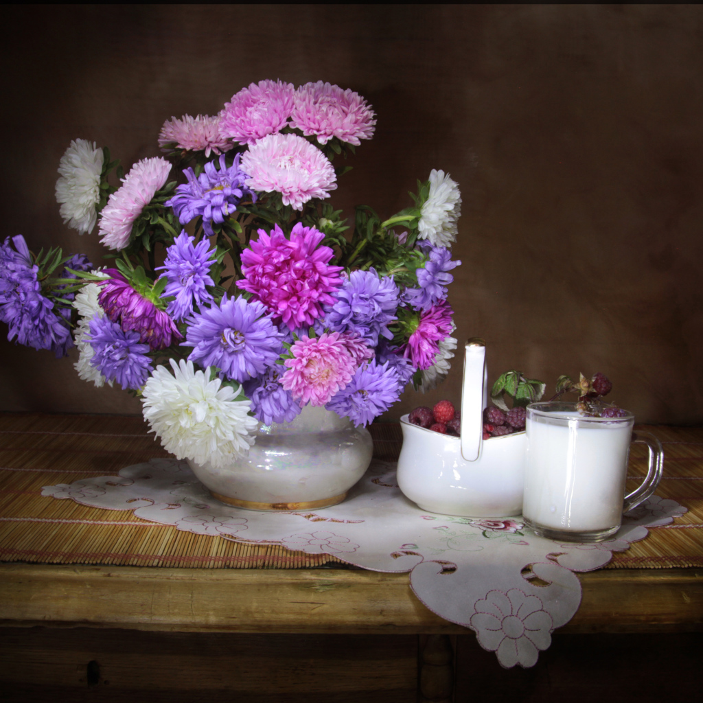 Букет разноцветных астр в вазе на столе с молоком и ягодами малины