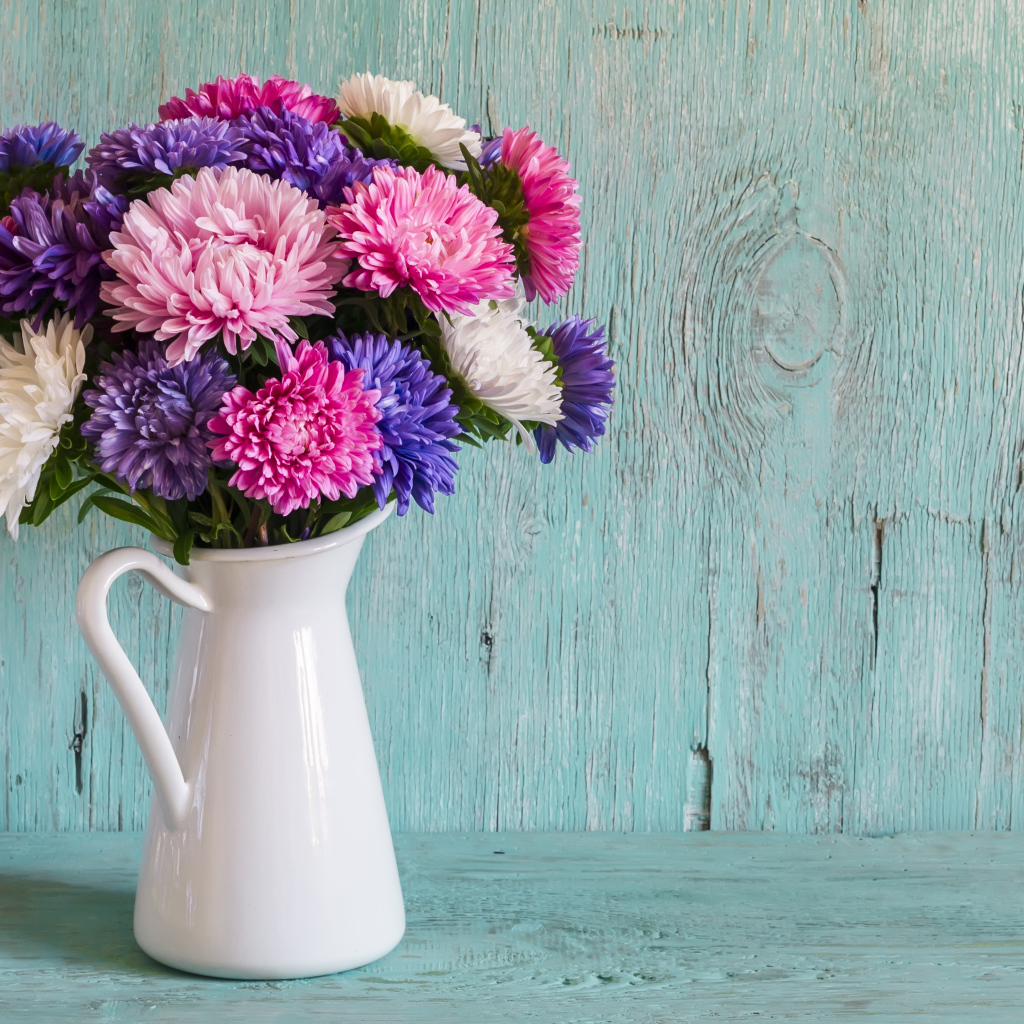 Разноцветные астры в вазе на деревянном фоне