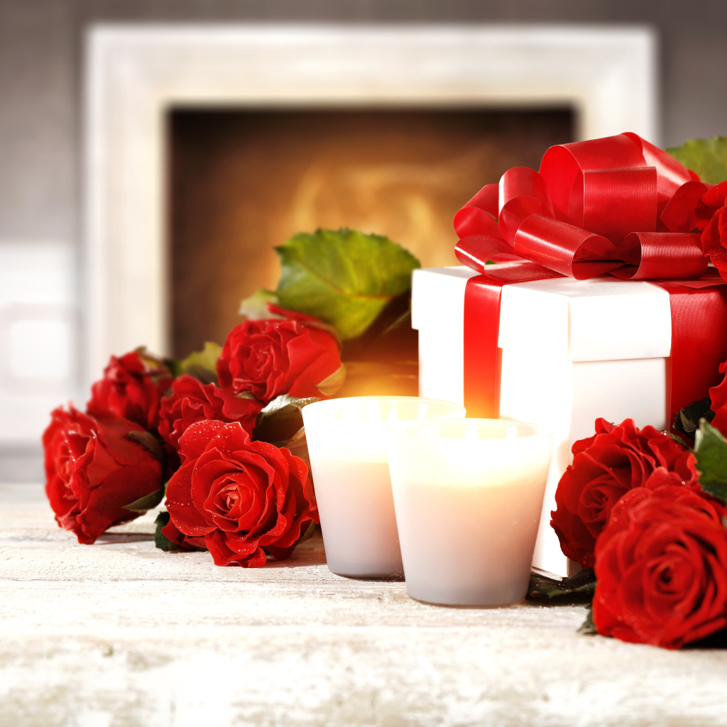 Красные розы с подарком и двумя зажженными свечами на столе