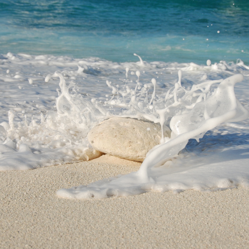 Белые морские волны бьются об камень на желтом песке