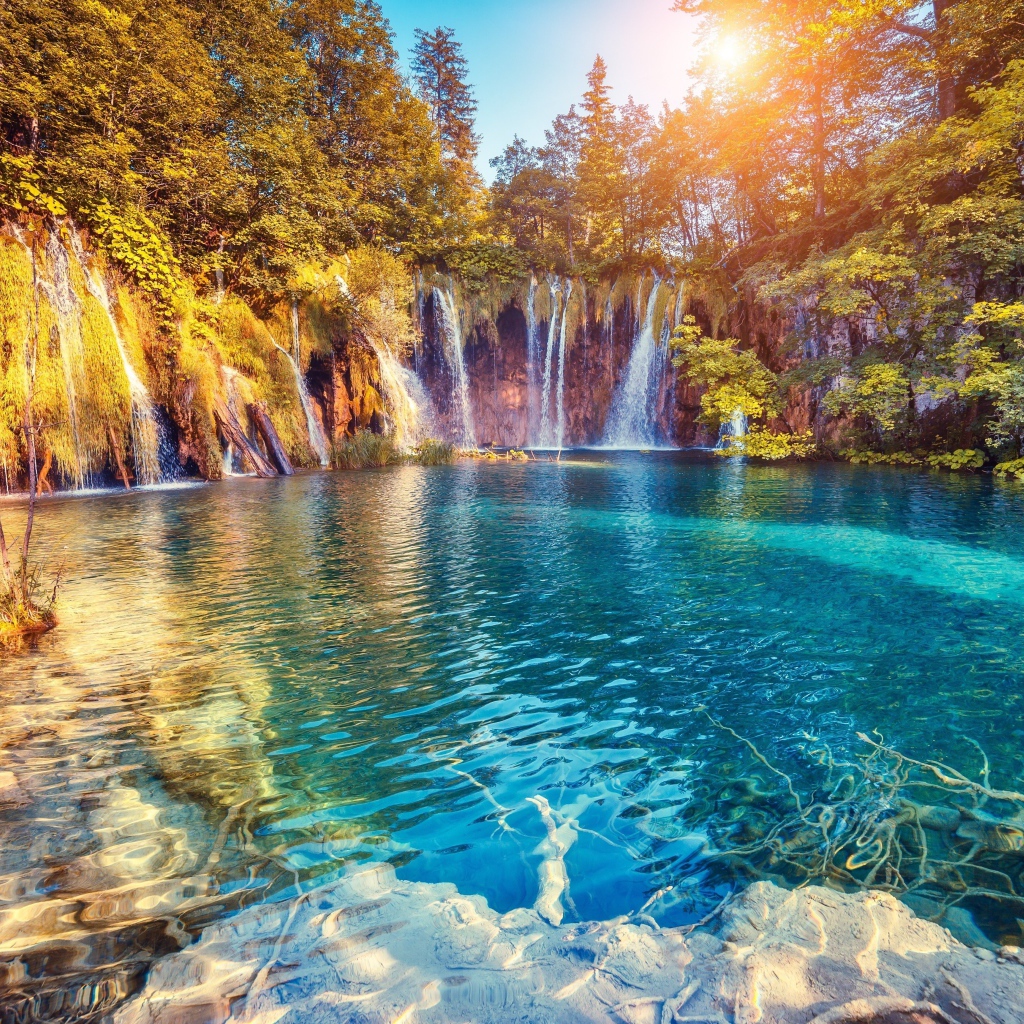 Водопад в лучах солнца стекает со скалы в реку