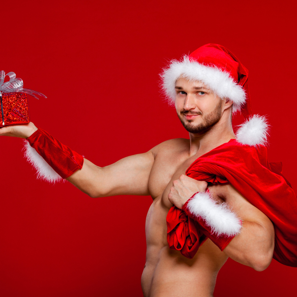 Мужчина в новогоднем костюме Санта Клауса с мешком и подарком в руке на красном фоне