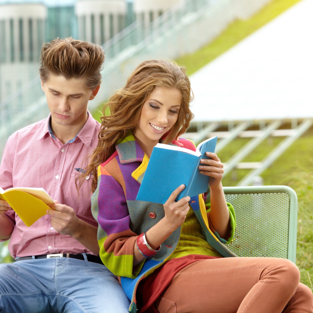A guy and a girl are reading books sitting on a bench