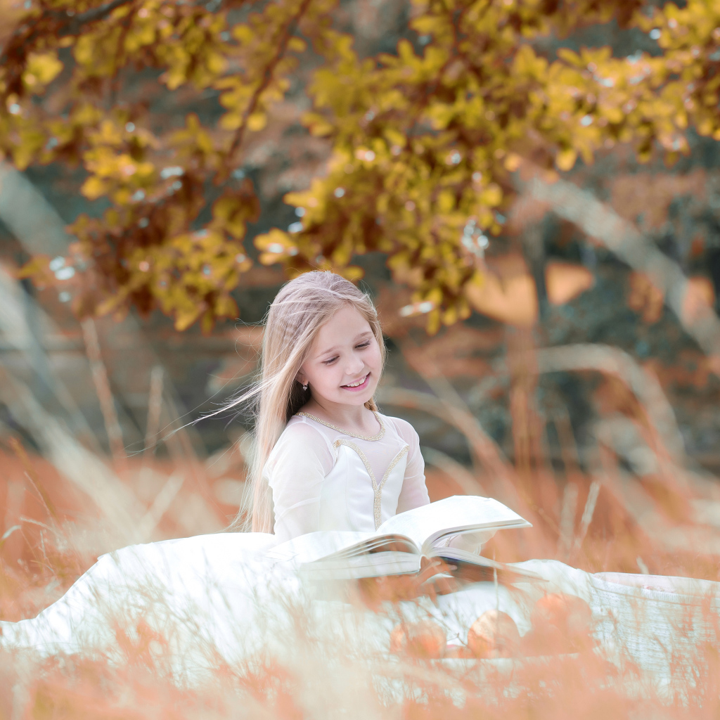 Девочка в красивом белом платье читает книгу на природе