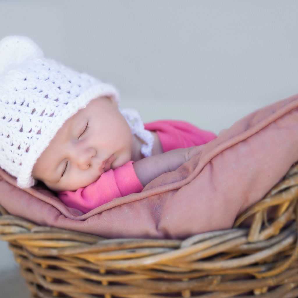 Маленький ребенок в белой шапке спит в корзине