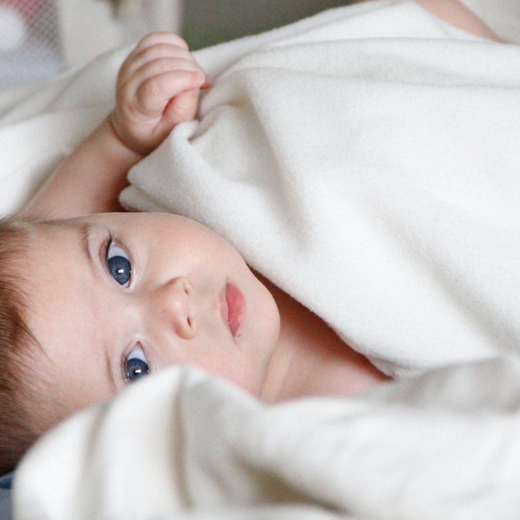 Маленький голубоглазый мальчик под белым покрывалом