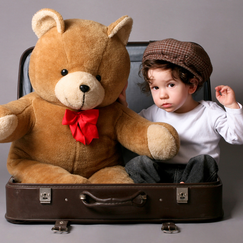 Маленький мальчик сидит в чемодане с плюшевым мишкой 