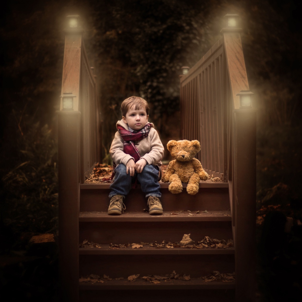 Маленький мальчик сидит с игрушечным мишкой на ступеньках