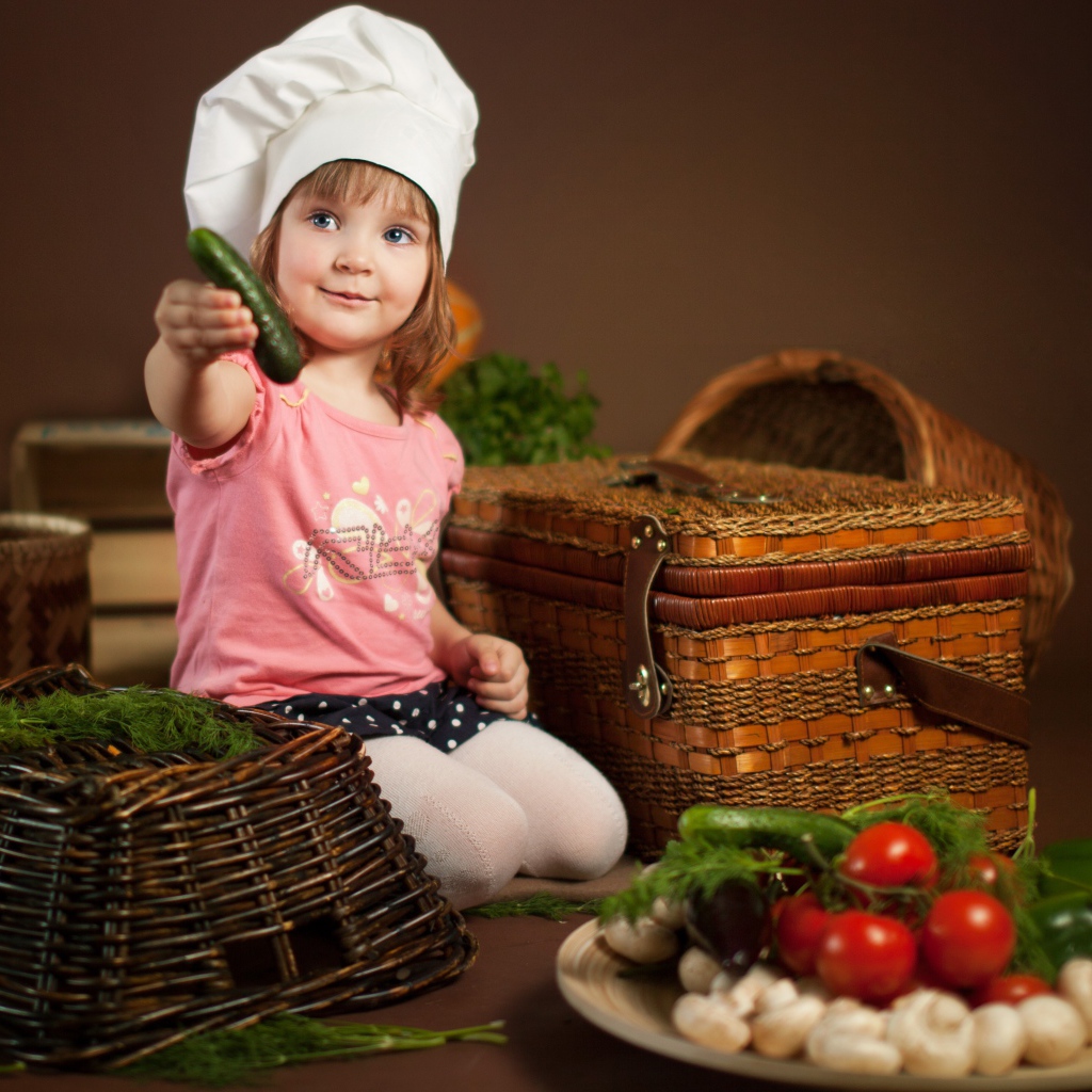 A little girl in a chef's hat with a cucumber in her hands