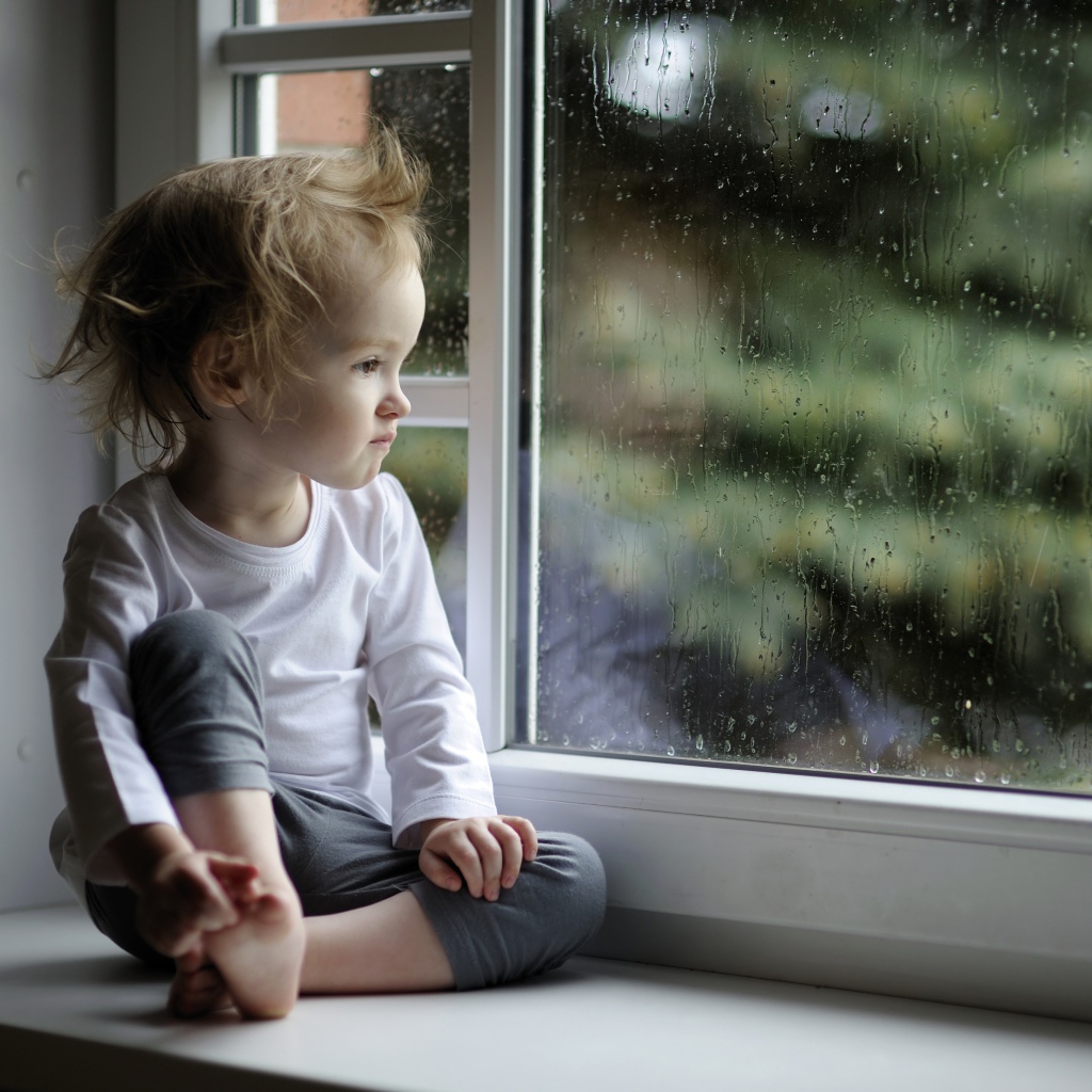 Маленькая девочка сидит на подоконнике у окна