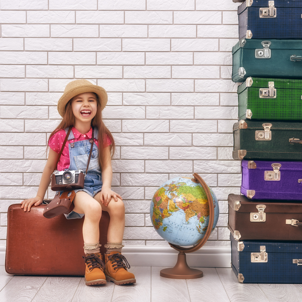 Маленькая девочка с фотоаппаратом сидит на чемодане