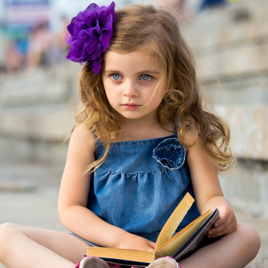 Маленькая девочка с цветком в волосах сидит на ступенях