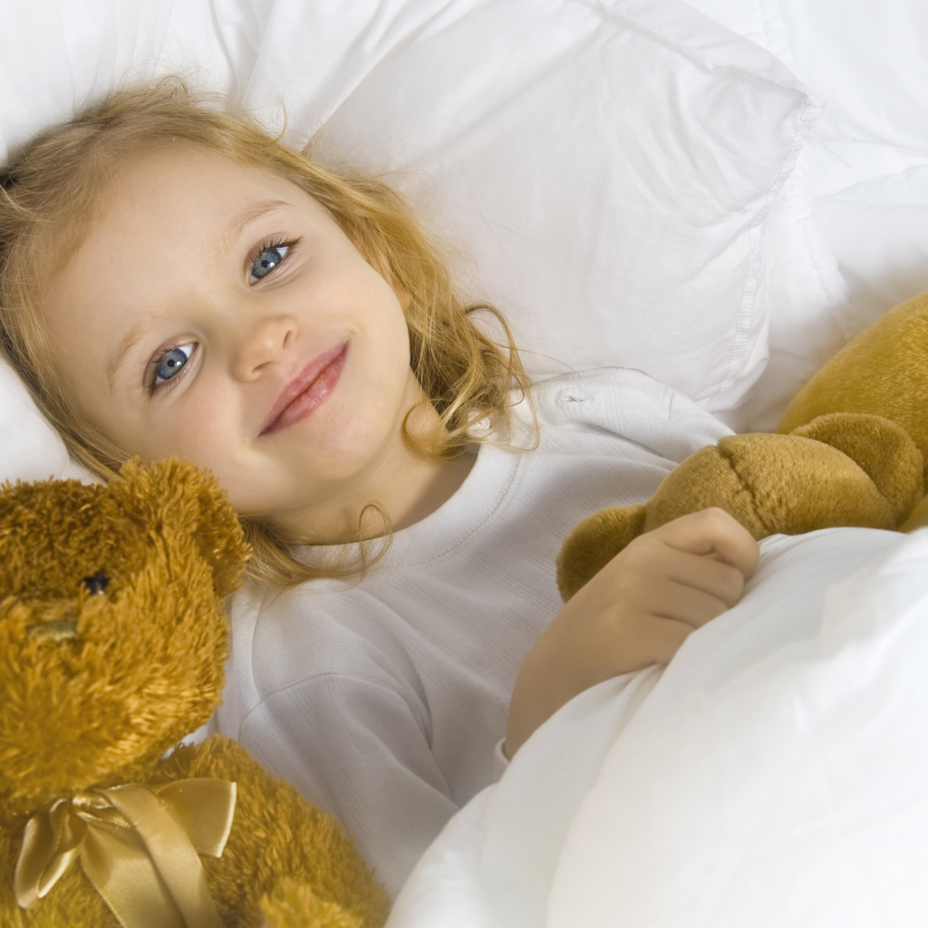 Милая голубоглазая девочка с мягкими игрушками лежит под одеялом