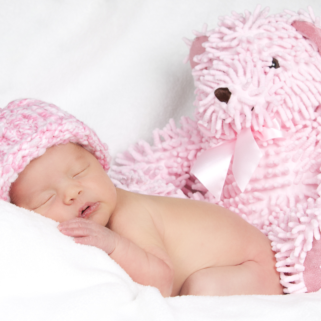 Спящий грудной ребенок в шапке с большим розовым медведем