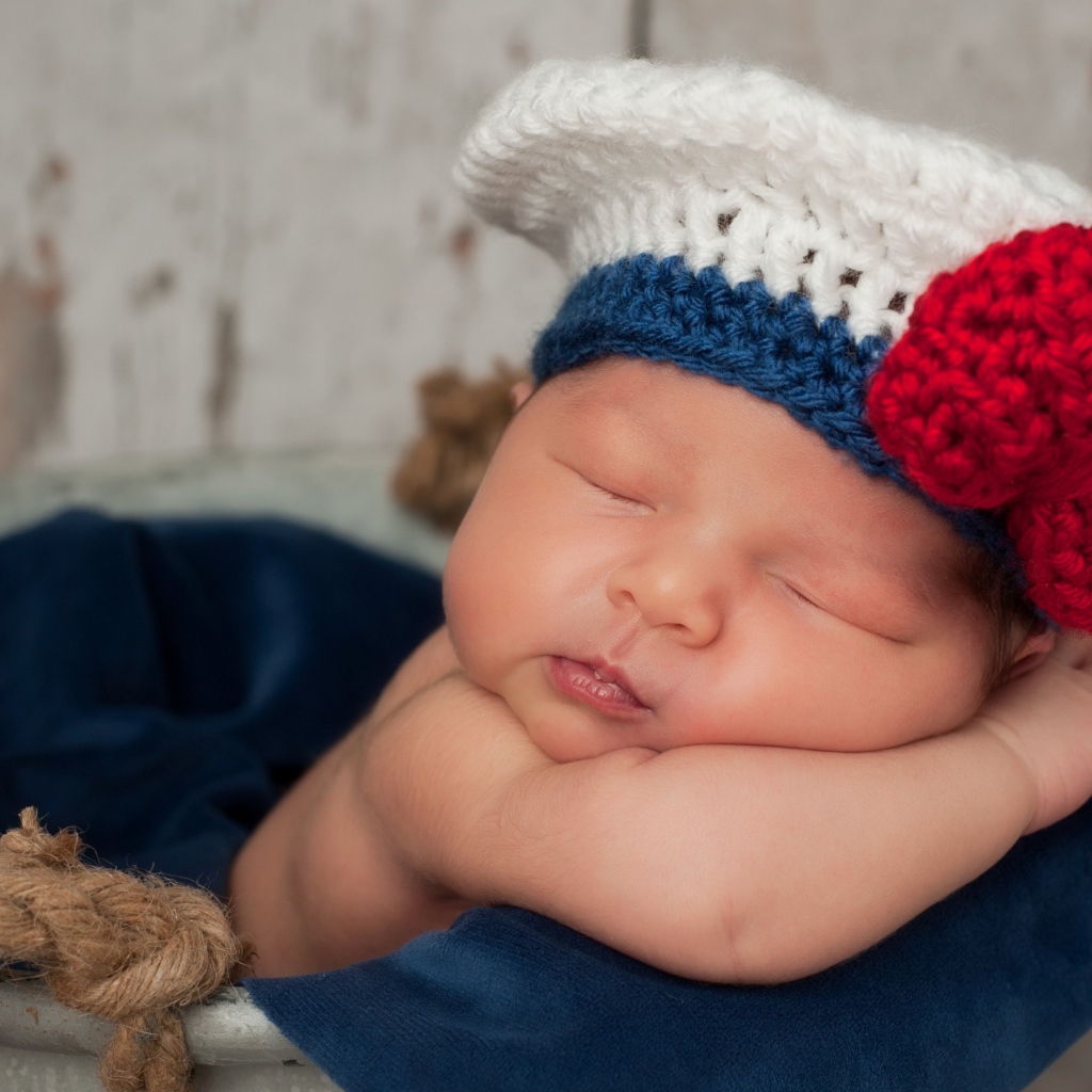 Спящий грудной ребенок в вязаной шапочке с красным бантом