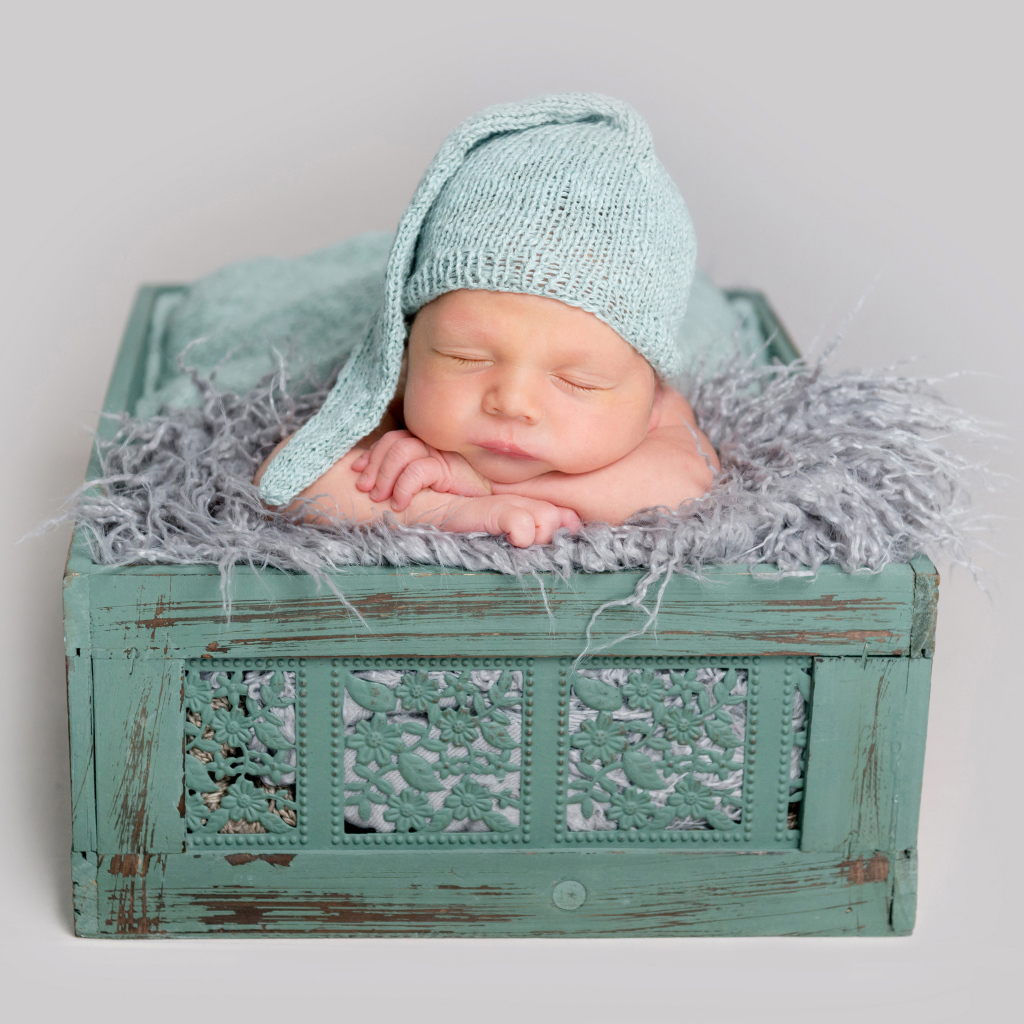 Спящий ребенок в зеленом ящике на сером фоне