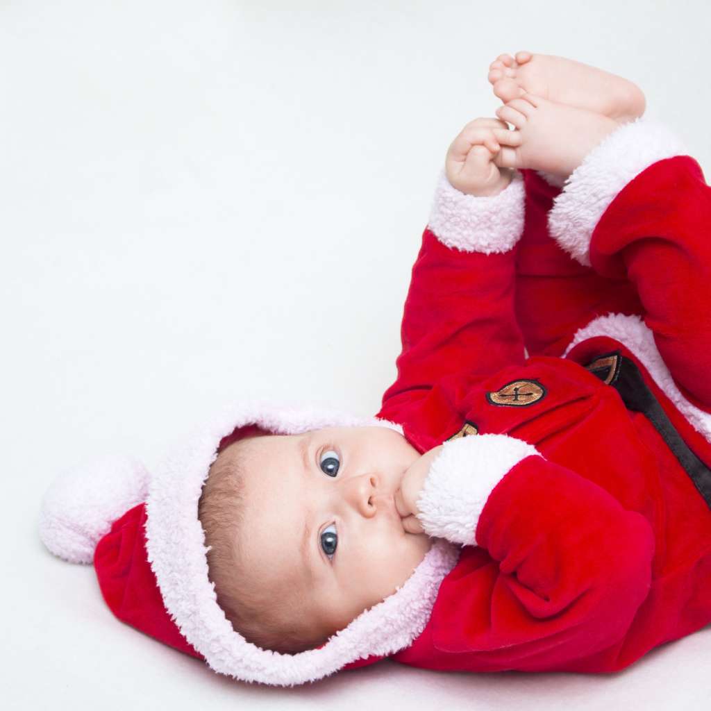 Маленький ребенок в красном новогоднем костюме на сером фоне