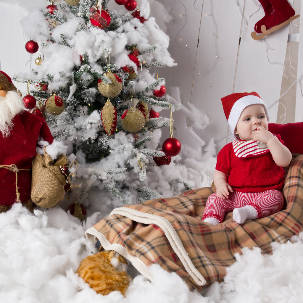 Маленький ребенок в санях у елки с дедом морозом на Новый год 