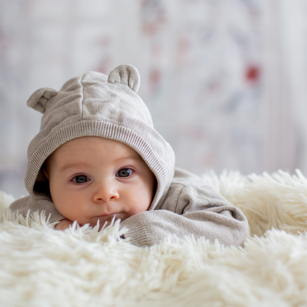 Маленький ребенок лежит на белом меховом покрывале 