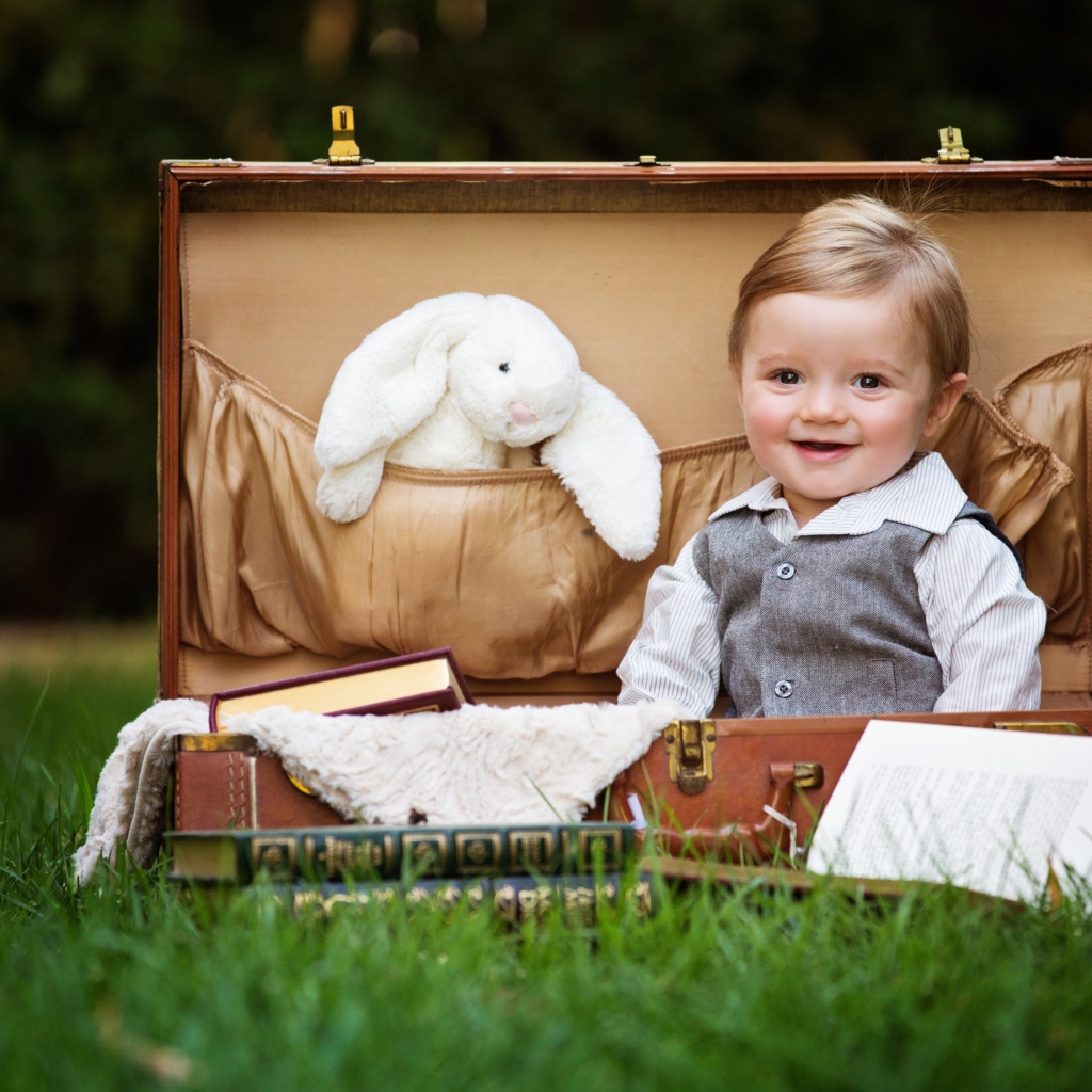 Улыбающийся мальчик сидит в чемодане с книгами