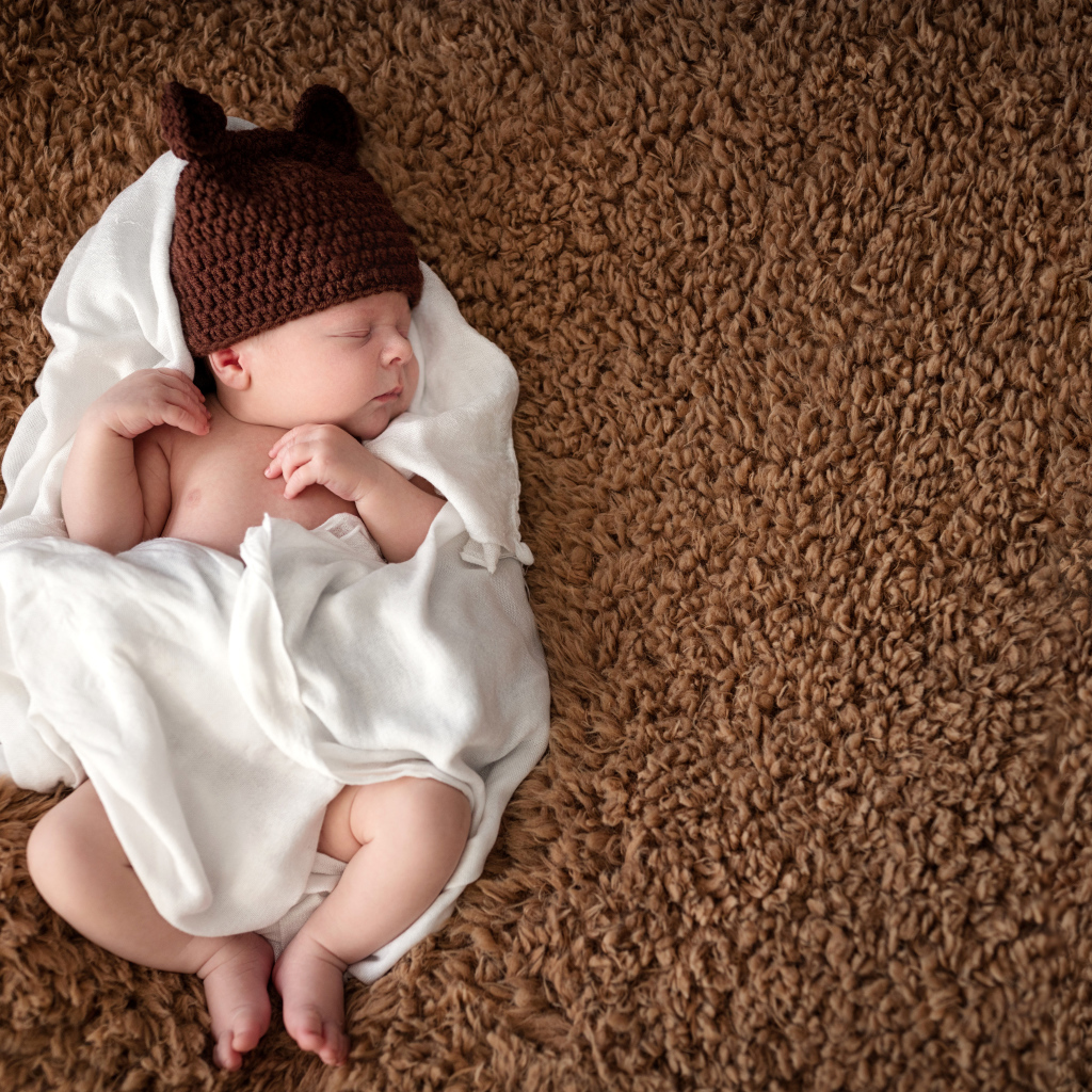 Младенец в коричневой вязаной шапке в белом покрывале 