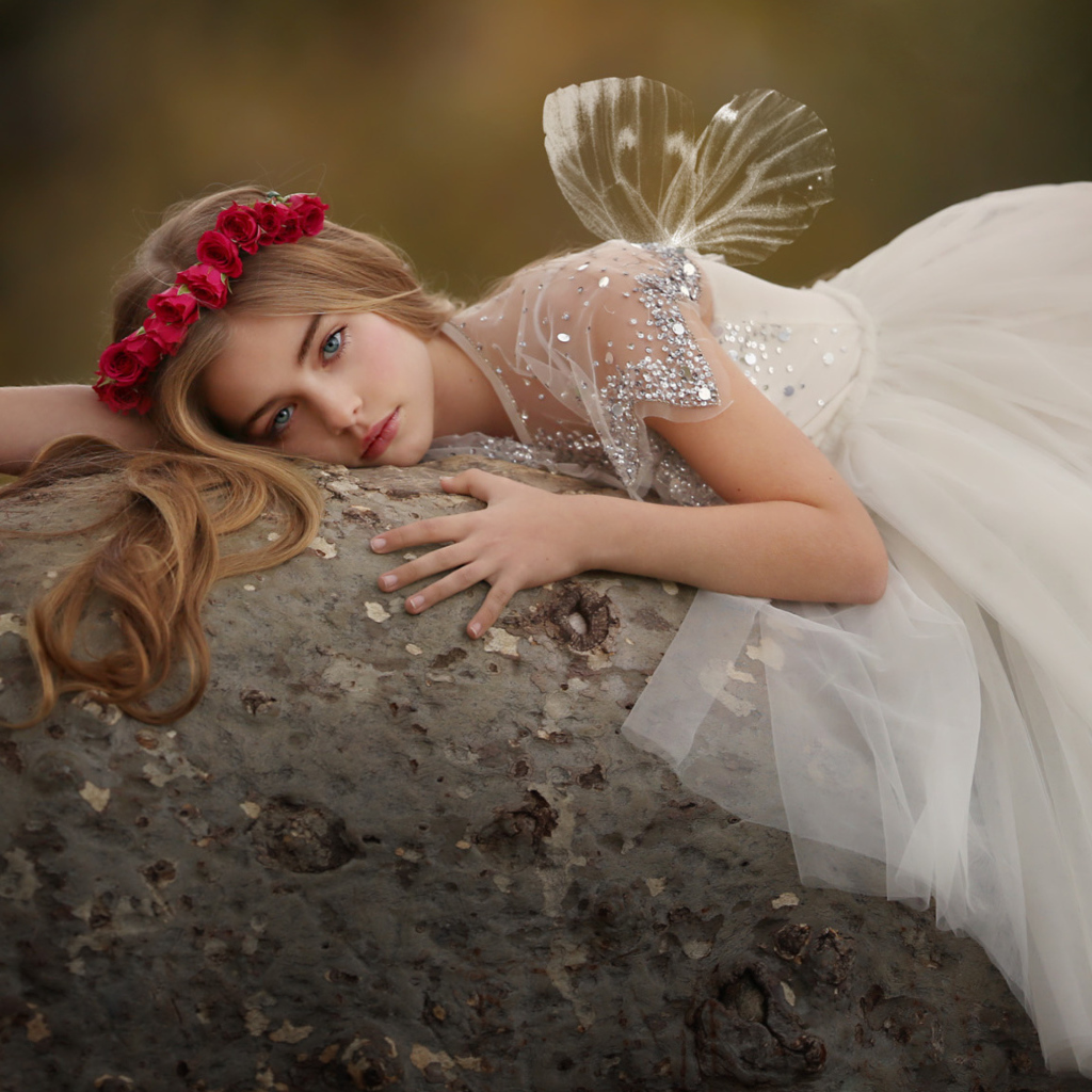 Красивая маленькая девочка в белом платье лежит на камне