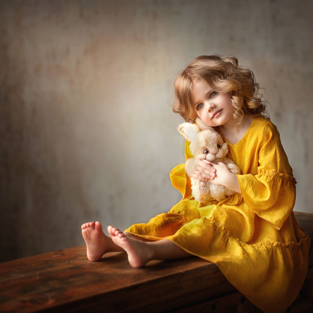 Красивая маленькая девочка в желтом платье с игрушкой