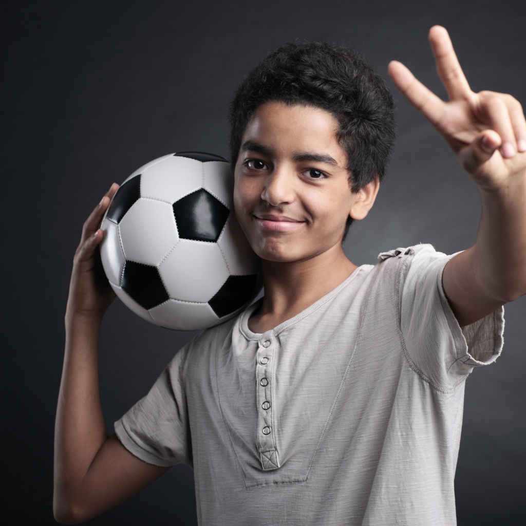 Мальчик с футбольным мячом на плече на сером фоне