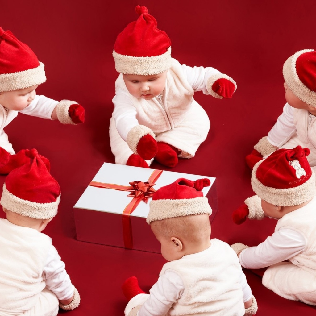 Младенцы в новогодних костюмах с подарком на красном фоне