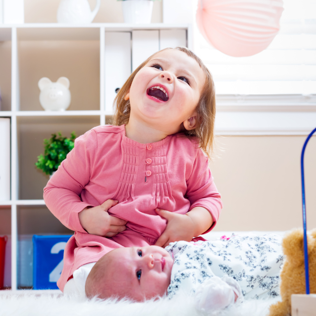 Смеющаяся маленькая девочка с младенцем