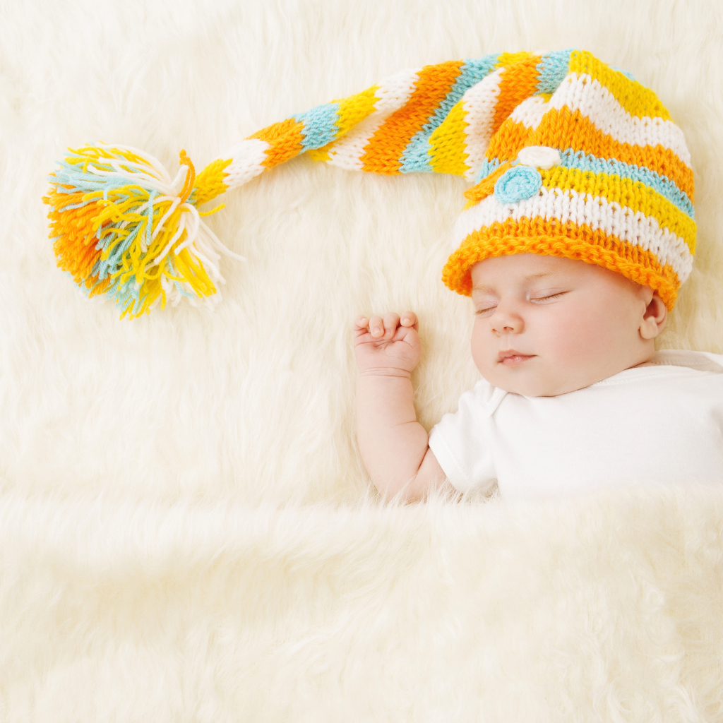 Маленький спящий под меховым покрывалом малыш в вязаной шапке