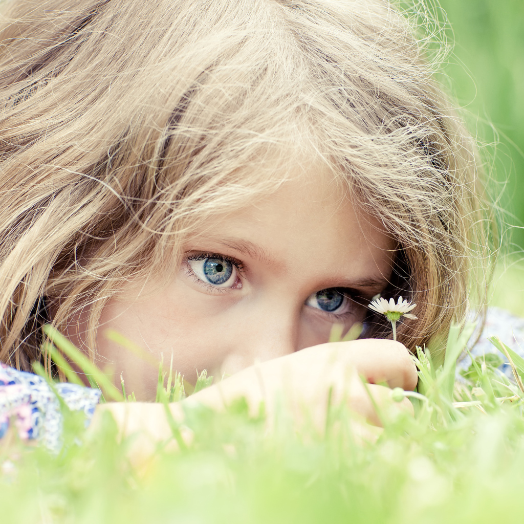 Маленькая голубоглазая девочка на траве с ромашкой