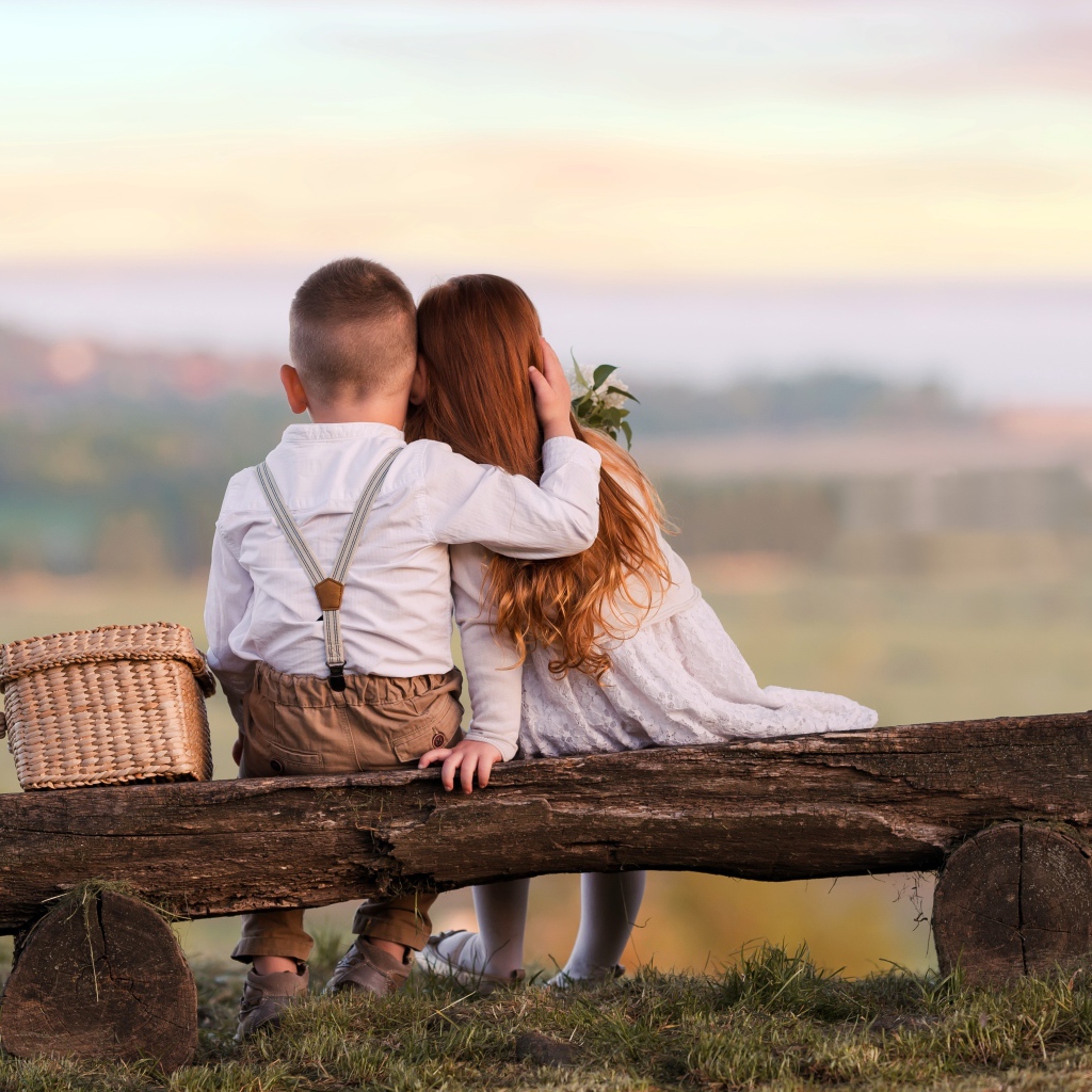 Маленькие мальчик и девочка обнимают друг друга на лавке
