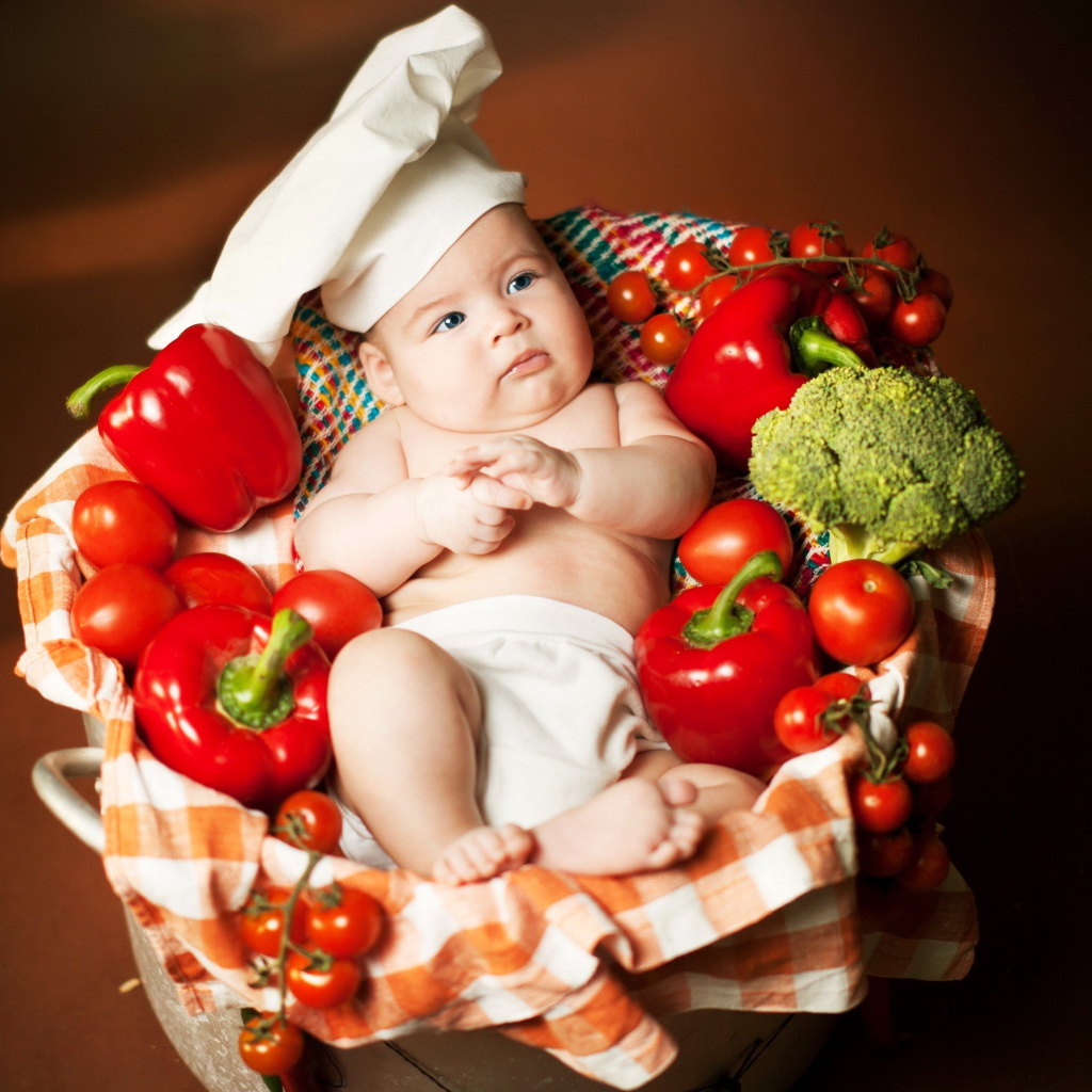 Маленький мальчик в костюме повара в корзине с перцем и помидорами