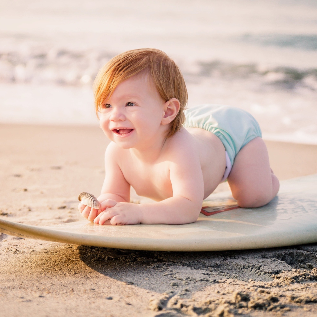 Маленький мальчик на доске для серфинга на пляже
