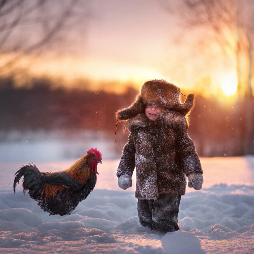 Маленький мальчик с петухом на снегу зимой