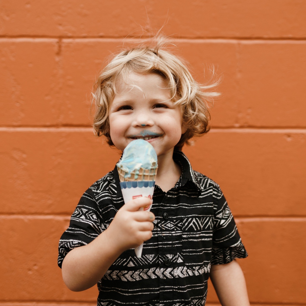 Маленький мальчик с мороженым в руках у стены
