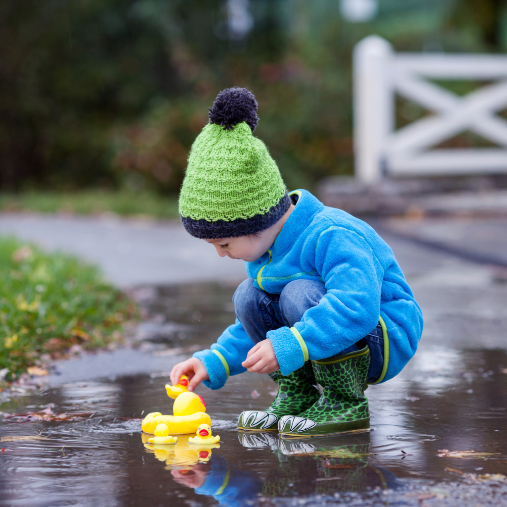 Маленький мальчик с резиновыми уточками в луже осенью