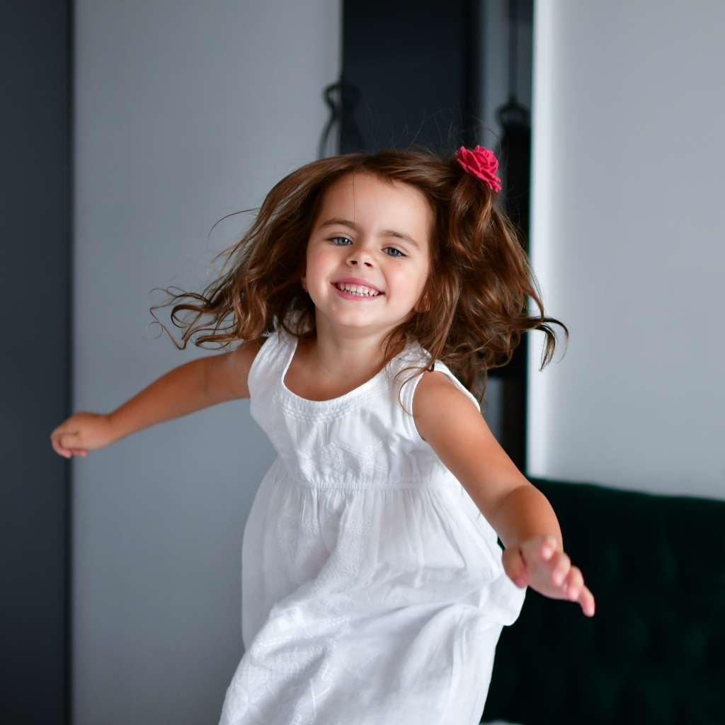 Маленькая веселая девочка в белом платье
