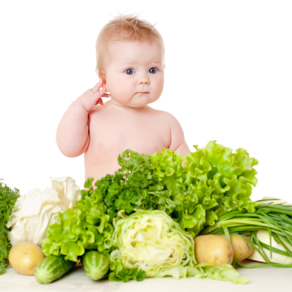 Маленький ребенок с овощами и зеленью на белом фоне
