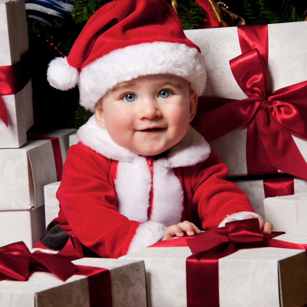 Маленький забавный голубоглазый ребенок в костюме Санты сидит на подарках