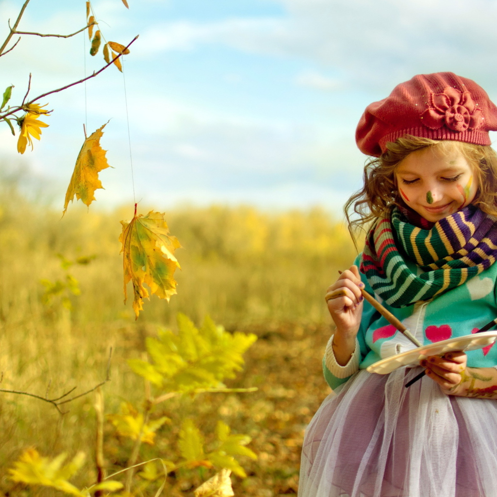 Маленькая девочка рисует красками на листьях осенью 